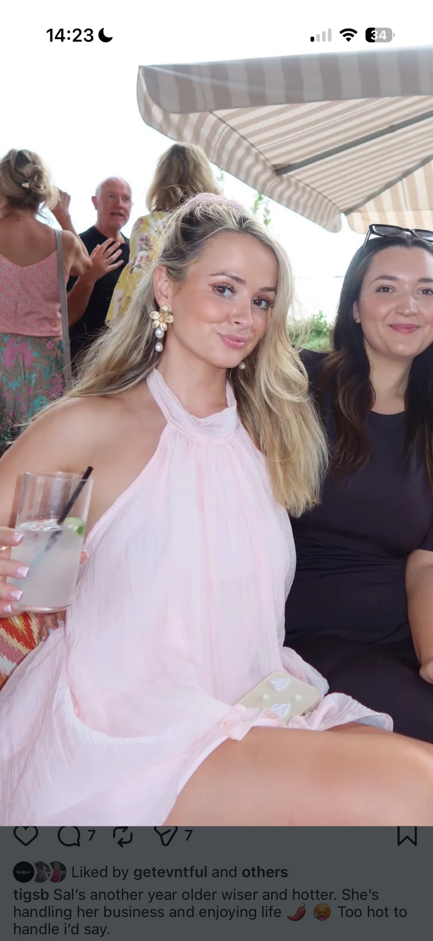 Birthday guest in a pink dress with a cocktail under a striped parasol